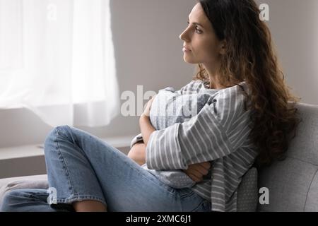 Woman sit on sofa gazing out window in deep contemplation Stock Photo