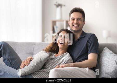 Portrait of couple looking at camera laughing, relaxing on couch Stock Photo
