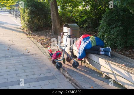A homeless man sleeps on a park bench with his walker in front of him Stock Photo
