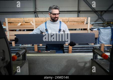 Man in safety glasses cuts aluminum profile on modern equipment Stock Photo