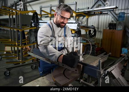 Middle-aged worker works on a modern machine with metal part Stock Photo