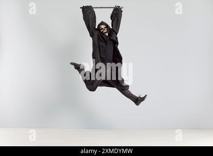 Man in grim reaper death costume jumping with scythe in his hands and having fun on Halloween party. Stock Photo