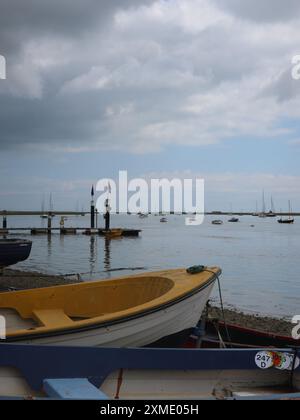 The Suffolk coast: a dinghy moored on the shingle at Orford Quay with a view towards the pier and boats further out in the estuary. Stock Photo