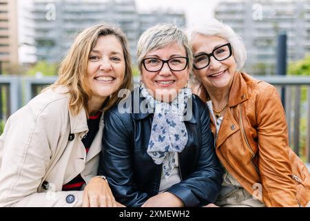 Portrait of three mature retired women smiling at camera sitting outside. Stock Photo