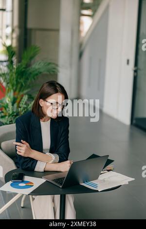 Young businesswoman focused on laptop, analyzing charts in a modern office setting Stock Photo