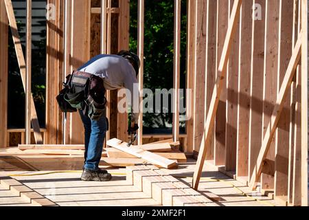 Construction worker in toolbelt and hard hat working with a hammer on new house construction framing, summer construction season Stock Photo