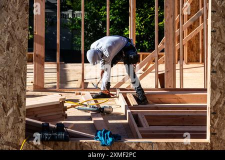 Construction worker in toolbelt working with a hammer and pry bar on new house wood construction framing, summer construction season Stock Photo