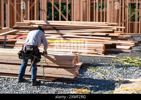 Construction worker in toolbelt and hard hat working with a tape measure on new house wood construction framing, summer construction season Stock Photo