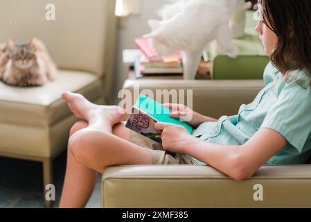 A child wearing a light green shirt and khaki shorts is seen relaxing on a beige sofa, using a green overlay to read a book more easily. This moment captures the child's dedication to overcoming dyslexia through the use of reading aids, highlighting the importance of accessible education. The scene is set in a comfortable home environment, emphasizing relaxation and focused learning. Ideal for themes related to childhood, dyslexia, educational aids, summer activities, and inclusive education. Stock Photo