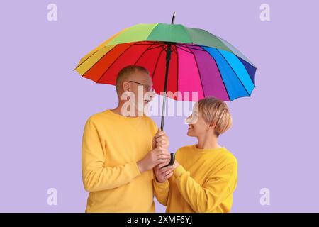 Mature couple with rainbow umbrella on lilac background Stock Photo