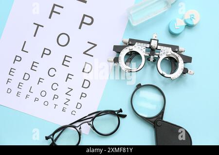 Optical trial frame with eye test chart, eyeglasses and magnifier on blue background Stock Photo