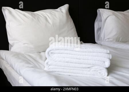 Two pillows on a bed covered with white linen, a sheet, towels. Bedroom in a hotel. Stock Photo