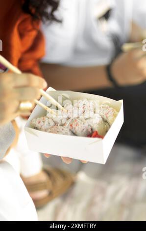 Crop shot from above of man and woman taking sushi with chopsticks from carton box. Stock Photo