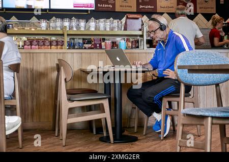 Man using a laptop and wearing headphones in cafe. England UK Stock Photo