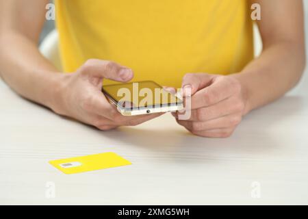 Man with ejector opening SIM card tray in smartphone at white wooden table, closeup Stock Photo