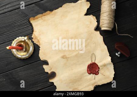 Sheet of old parchment paper with wax stamp, twine and candle on black wooden table, top view Stock Photo