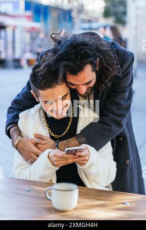 Young man embracing his boyfriend using smartphone at a cafe Stock Photo