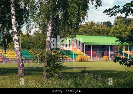 A soccer field with green bleachers and trees in the foreground on a sunny day. Stock Photo