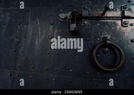 A close-up shot of a rustic metal door featuring a heavy-duty lock and a circular handle ring, showcasing the aged and weathered texture of the metal Stock Photo