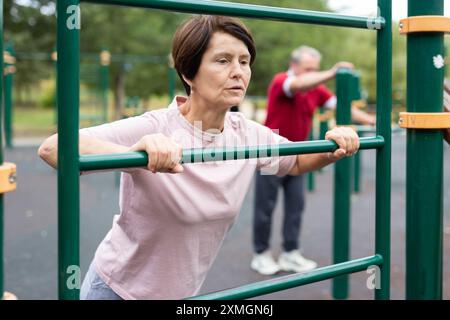 Mature woman doing push-ups from the crossbar on outdoor sports ground Stock Photo