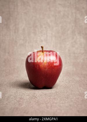 Single red apple standing on a textured beige background representing healthy food and lifestyle Stock Photo