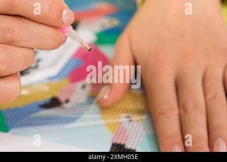 A close-up of a hand placing crystals on a canvas for a diamond painting project. Diamond Mosaic Stock Photo