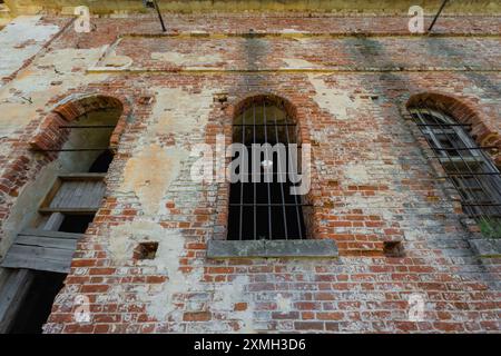 Close-up of an old brick wall featuring three arched windows with iron bars. The wall shows signs of wear and weathering, adding a rustic and historic Stock Photo