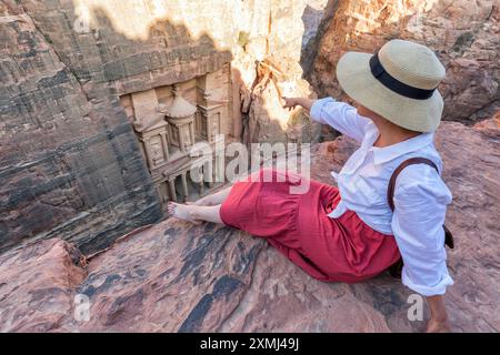 Woman traveler sitting on carpet viewpoint in Petra ancient city looking at the Treasury or Al-khazneh, famous travel destination of Jordan and one of Stock Photo