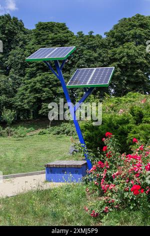 Solar panels in a city park for charging mobile phones. Rose bushes. Green trees in the distance. Stock Photo