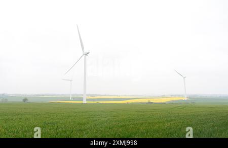 An electricity generating windmills on the yellow and green field against cloudy blue sky  in England Stock Photo