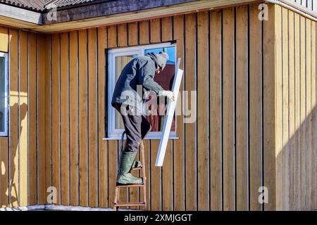 Standing on stepladder, roofing contractor installs metal window slopes on facade side. Stock Photo