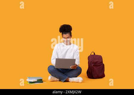 Young Woman Using Laptop While Sitting On Yellow Background Stock Photo