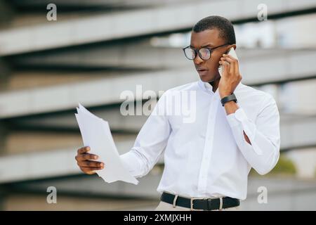 Businessman Talking On Phone While Reviewing Documents Outdoors Stock Photo