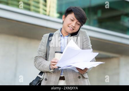 Businessman Reviewing Documents While Talking on the Phone Outside Stock Photo