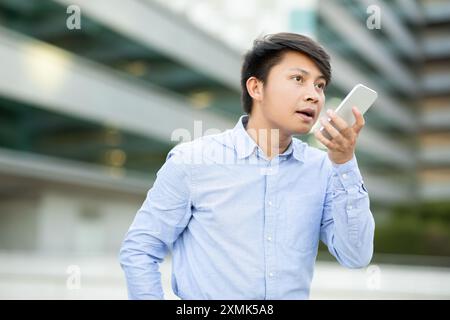 Man Speaking Into Smartphone on City Street During the Day Stock Photo