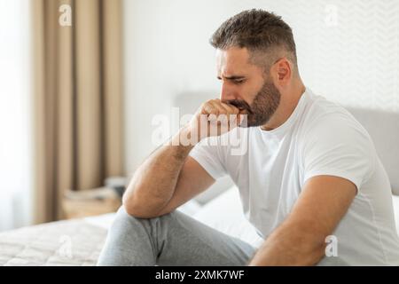 Man Sitting On Bed With Worried Expression In Home Stock Photo