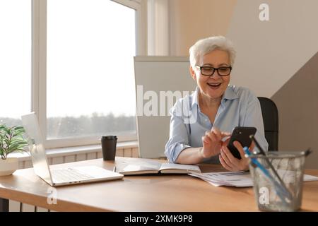 Confident middle aged senior woman euphoric winner with smartphone. Older mature lady looking at cell phone reading great news getting good result winning online bid feeling amazed. Winning gesture Stock Photo