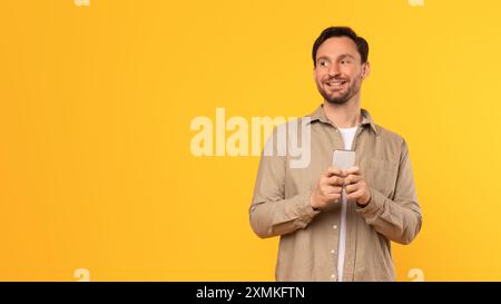 Happy Man Using Smartphone Against Yellow Background Stock Photo