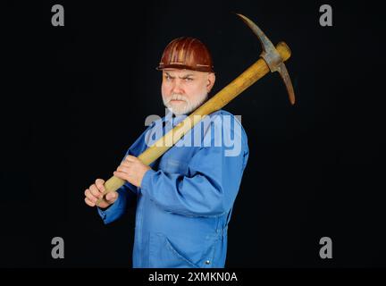 Serious builder man in uniform with pick-axe on shoulder. Mining industry. Mature coal miner with pickax. Male laborer with hand tool for digging, min Stock Photo