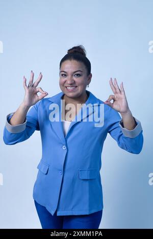 A successful businesswoman is wearing a stylish blue blazer and making a positive OK sign with her hand Stock Photo