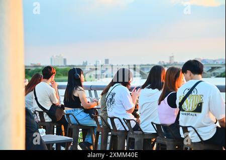 Taiwan - Jul 28, 2024: Tourists enjoy a picturesque sunset while dining at Dadaocheng Pier Plaza, a vibrant riverside spot in Taipei. Stock Photo