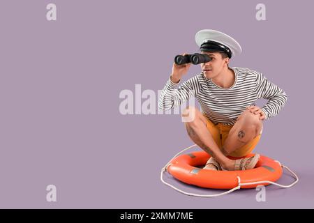 Young sailor looking through binoculars on ring buoy against lilac background Stock Photo