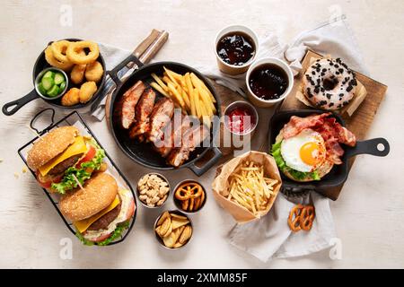 Various of american food, French fries, hamburgers, chips, popcorn, snacks and sauces on a white background, top view. Stock Photo