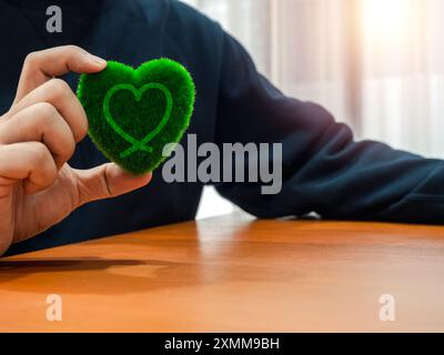 Donation, fundraising, love, charity, donate for help and earth care concept. Heart line graphic, hand draw style, on green grass heart shape, holding Stock Photo