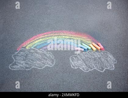 Sidewalk chalk drawing. A rainbow and clouds sky painted on the asphalt ...
