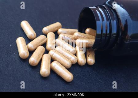 Several brown medicine capsules falling from the bottle packaging with close-up view on black background. Stock Photo