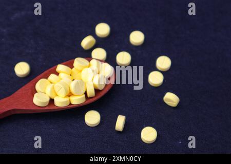 Yellow medicine tablets or vitamin C medicine in a wooden spoon and some scattered in close up view on black background. Stock Photo