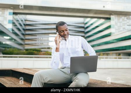 Man Talking on Phone While Working on Laptop Outside Building Stock Photo