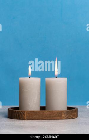 Two burning candles on wooden stand on blue background with copy space Stock Photo