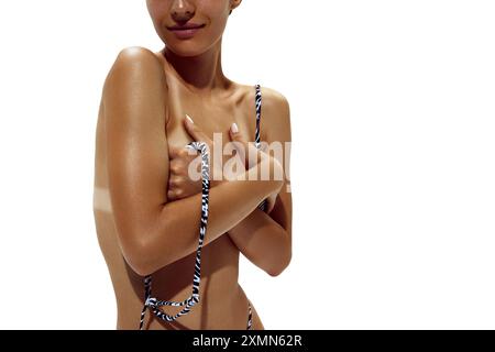 Woman adjusts her zebra-print bikini, revealing clear tan lines on her deeply tanned skin against white studio background. Stock Photo